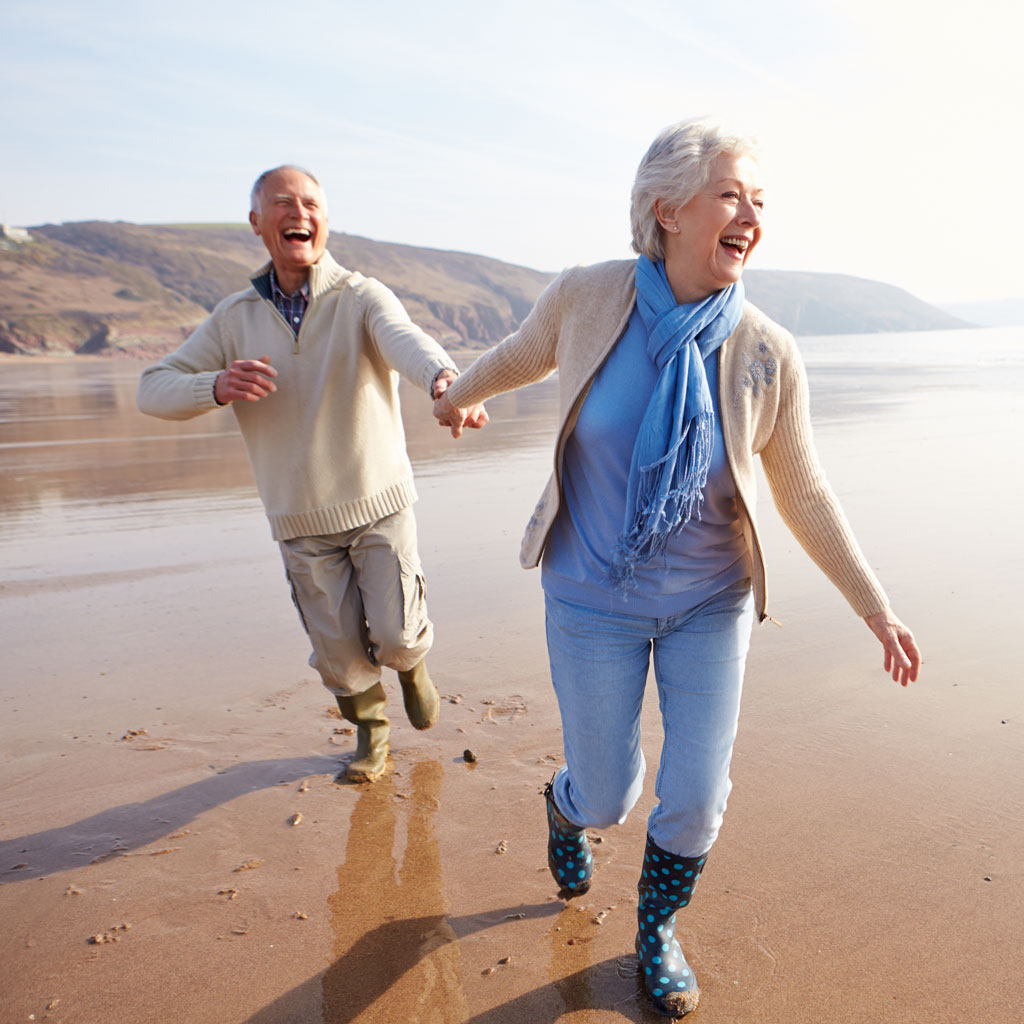 Älteres Paar läuft lachend über den Strand